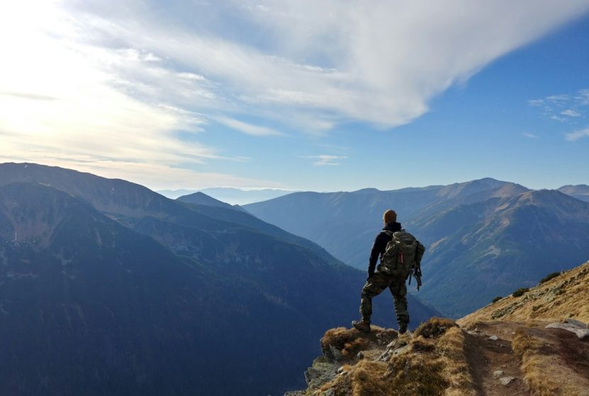 Htaking image of a solitary hiker, surrounded by towering mountains and dense forests, embarking on a winding, rugged trail that disappears into the horizon